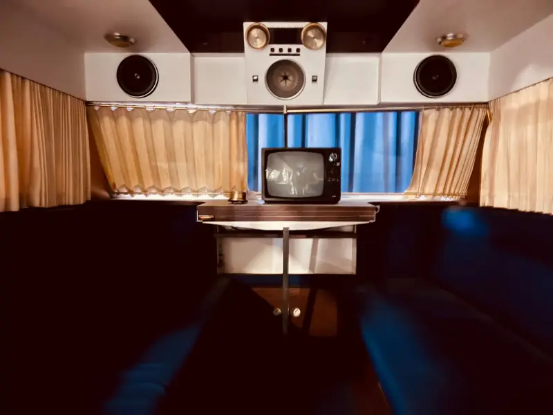 Interior of a vintage camper featuring retro TV, speakers, and cozy seating