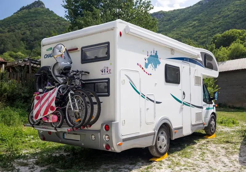 An RV with bicycles attached in a scenic outdoor setting, surrounded by mountains and greenery