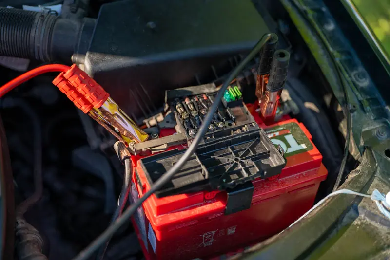 Close-up view of a car battery with red jumper cables connected, outdoors
