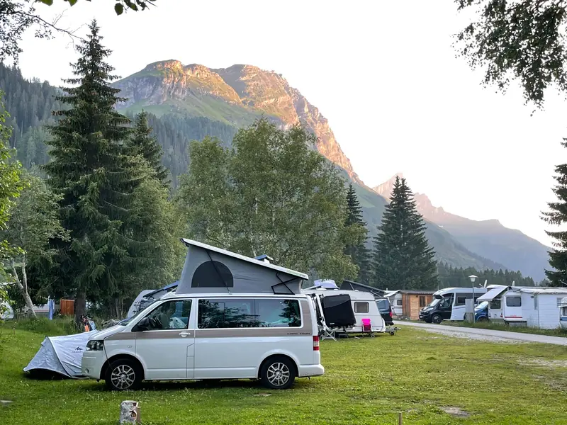 A serene camping site in Rheinwald, Switzerland with scenic mountains and parked camper vans