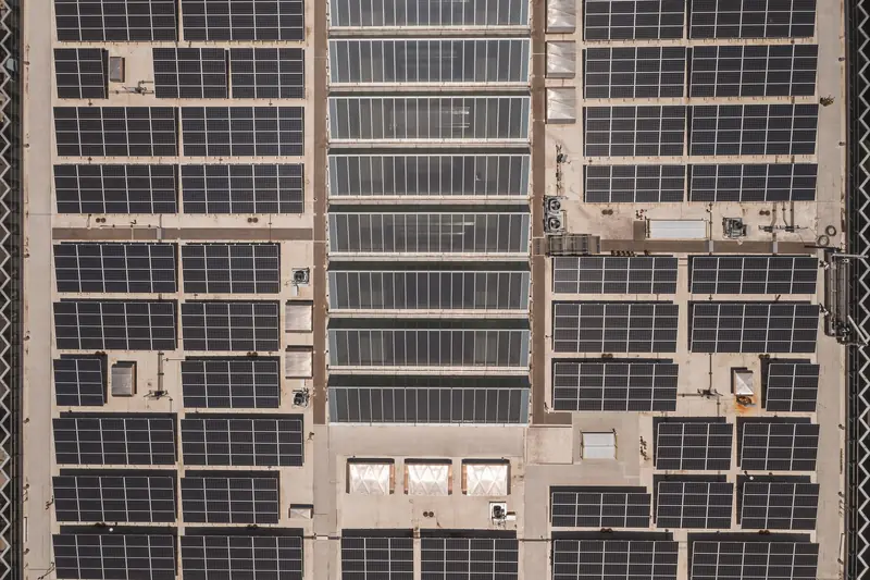 A high-angle drone shot capturing a grid of solar panels on a large industrial rooftop, showcasing renewable energy