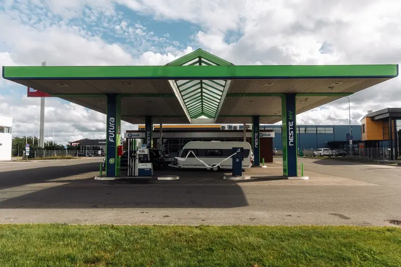 A modern gas station with a green canopy and parked camper van under a cloudy sky