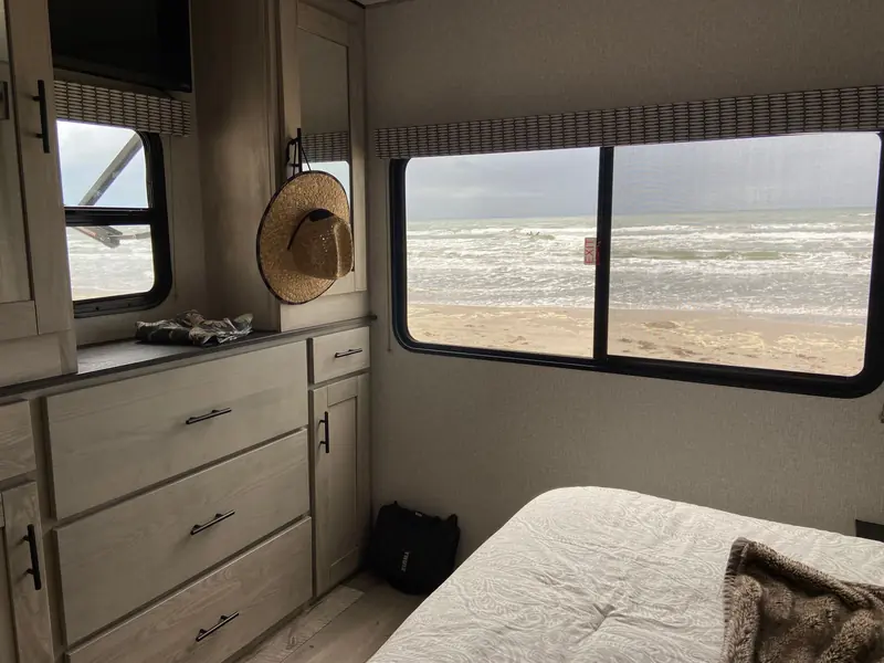 RV bedroom interior with ocean view through the window, featuring drawers and a sun hat