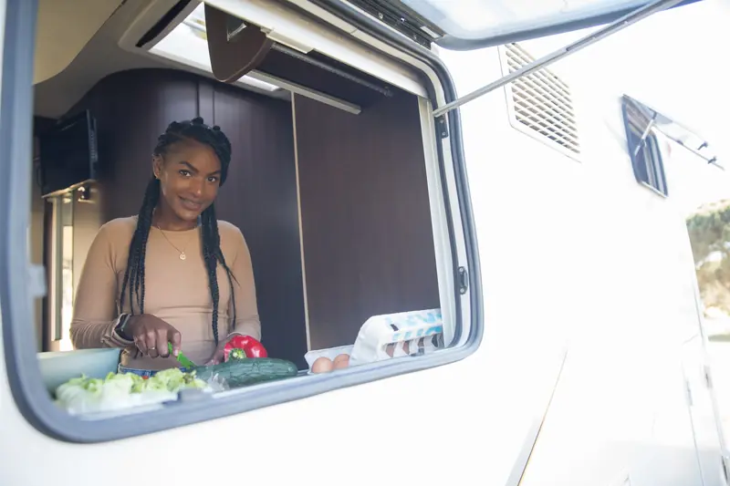 Young woman preparing food with fresh vegetables in a caravan kitchen. Outdoor lifestyle in a cozy mobile home