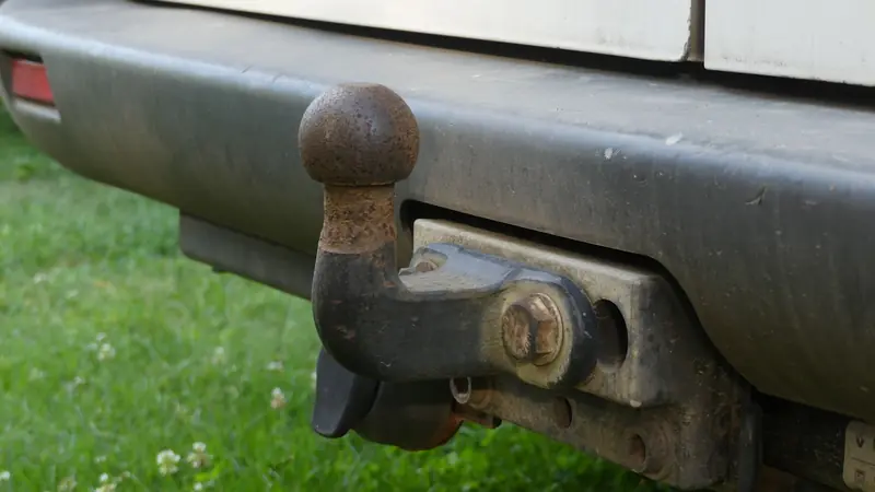 Close-up of a rusty tow hitch on the rear bumper of a vehicle against a grassy background