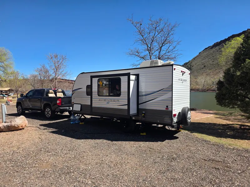 A scenic daytime camping setup with a caravan and truck by a lake in a natural setting