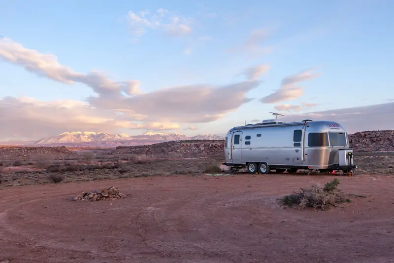 Silver trailer in desert landscape at sunset with mountains in the background