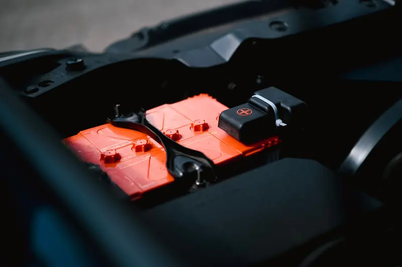 Detailed view of an orange car battery inside a vehicle's engine bay, highlighting its features
