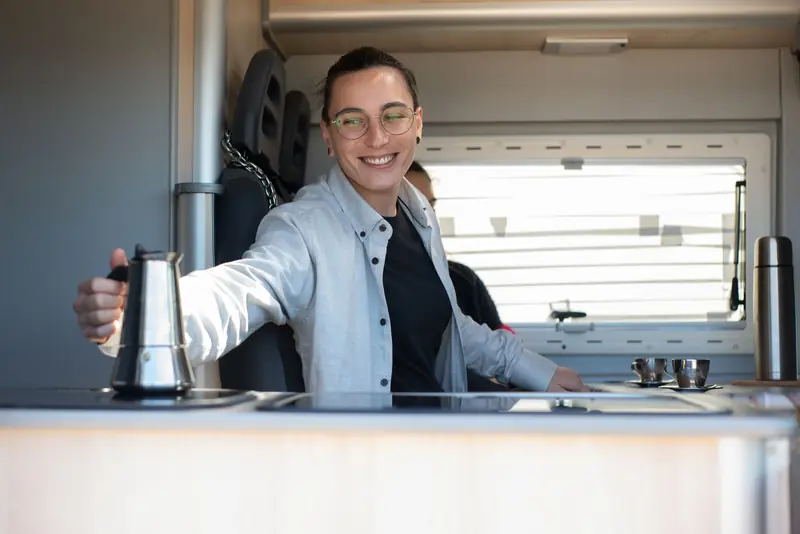 Caucasian person smiling while preparing coffee inside an RV kitchen in Portugal