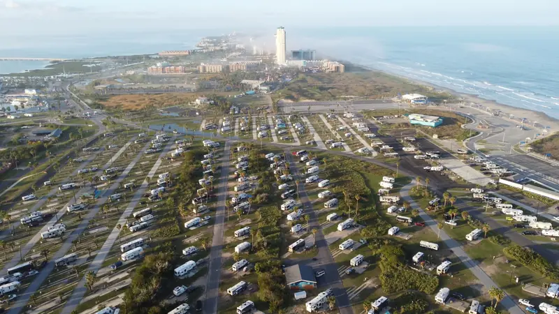 Aerial view of a coastal RV park near the ocean, showcasing numerous caravans and nearby resort buildings
