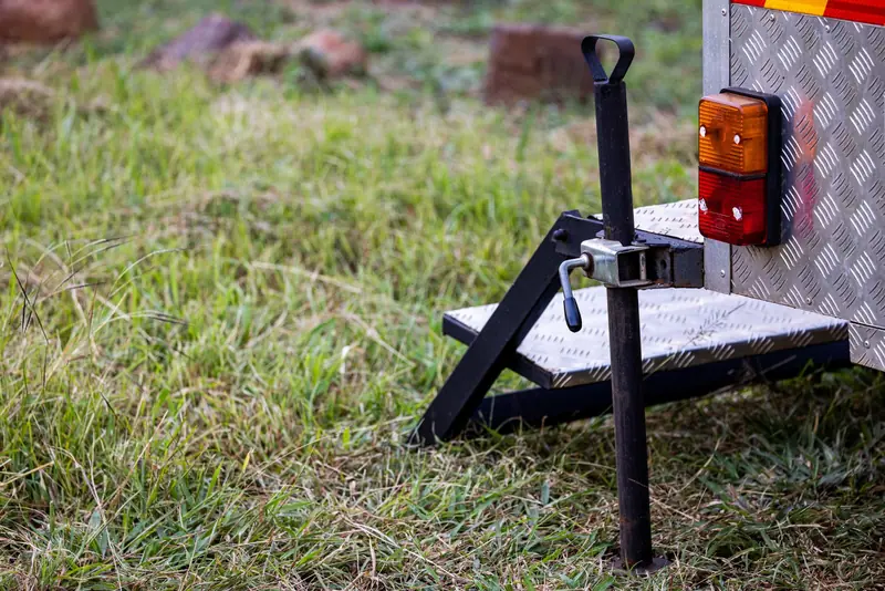 Close-up of a trailer hitch and jack on metal steps in a grassy field, ideal for outdoor or camping themes